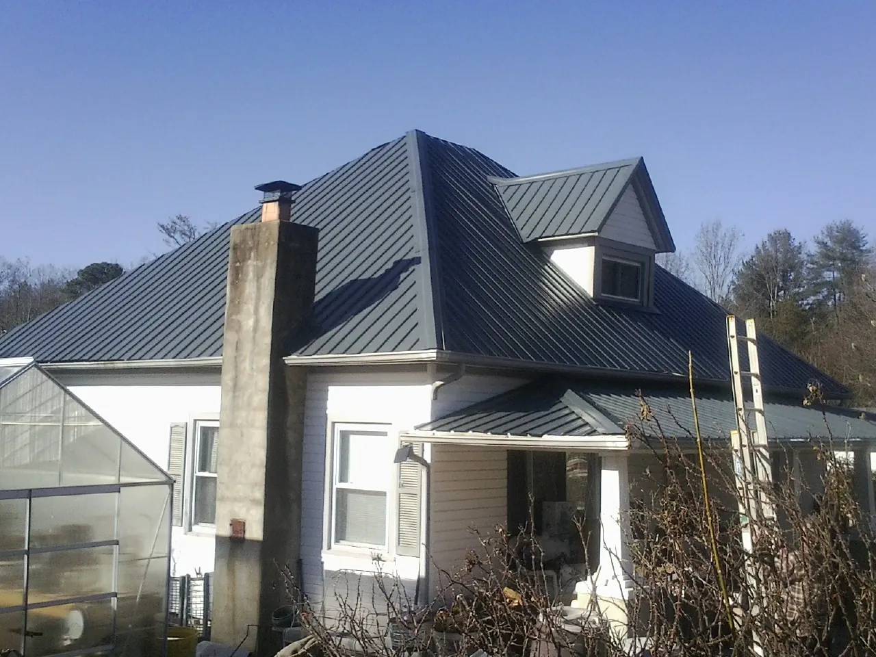 Dark blue standing seam metal roof on a white farmhouse with dormer — Slate & Tile Roof Repair by Roofing Brothers in Blanchard