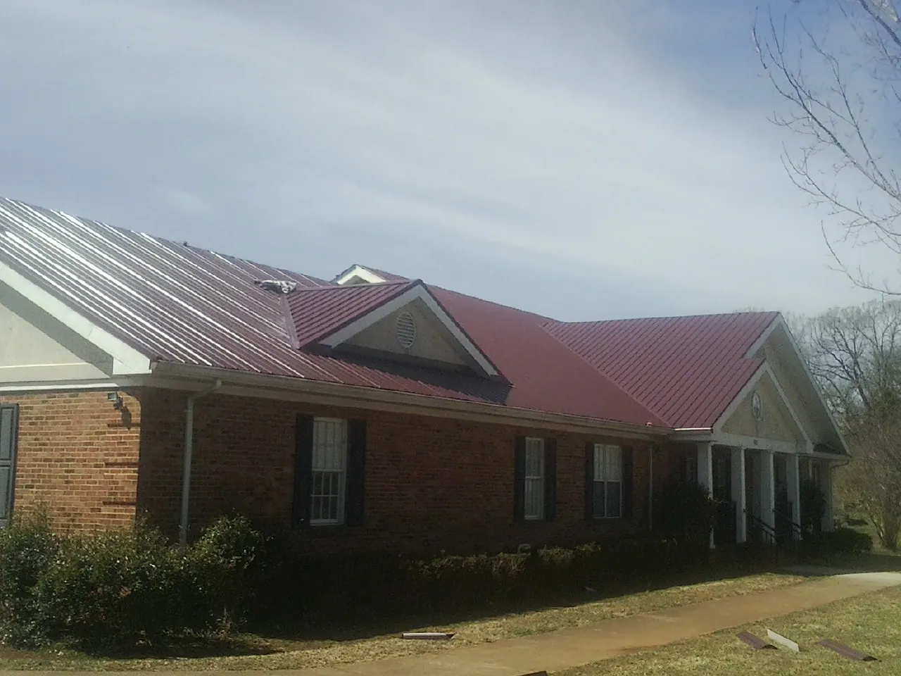 Red metal roof with gabled entries on a long brick building, from a Hail Damage Roof Repair job in Blanchard