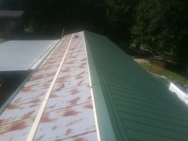 Old rusted panels beside newly installed green metal roofing — Wind Damage Roof Repair by Roofing Brothers in Blanchard