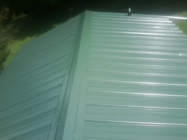 New green metal panels meeting at the ridge of a roof — Flat Roof Repair work by our crew in Blanchard