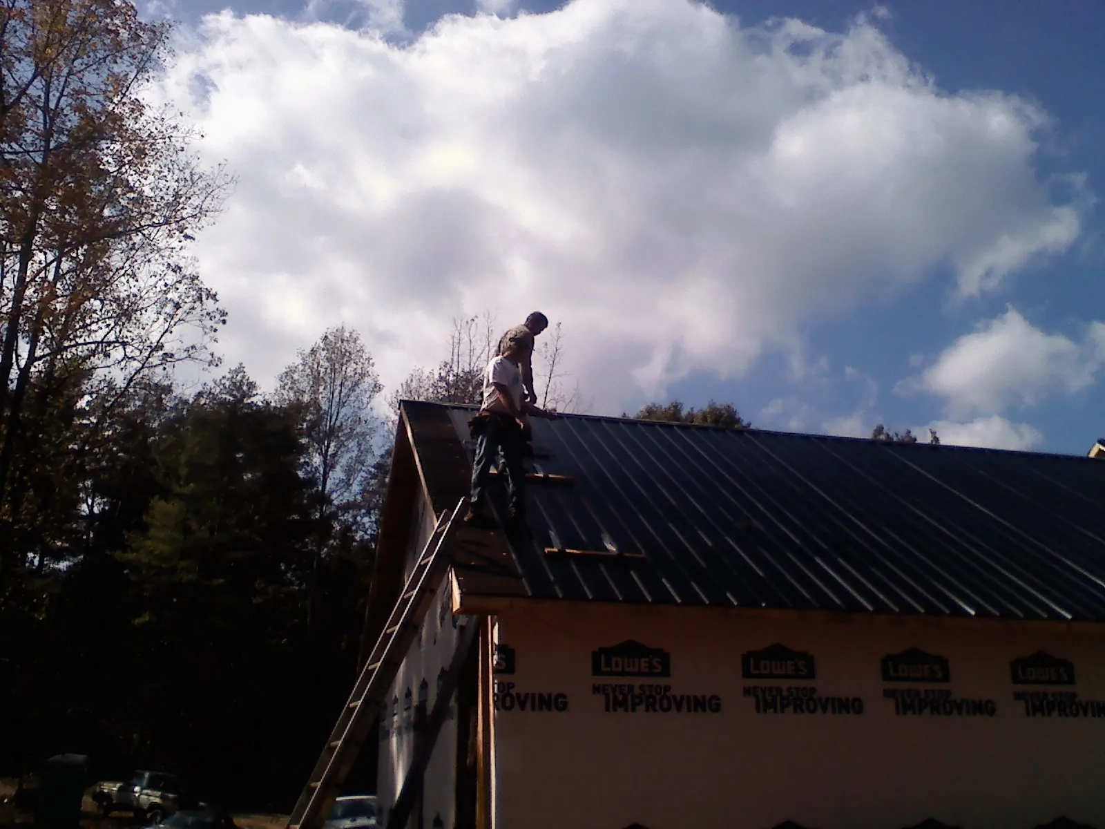 Roofer fastening dark metal panels high against a cloudy sky, from a Roof Inspection job in Blanchard