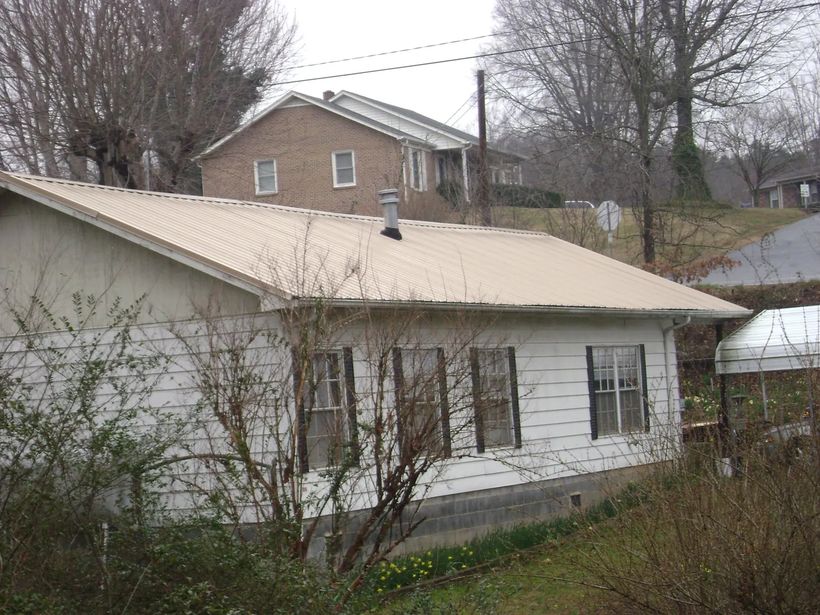 Tan metal roof on a white sided house set into a hillside — Commercial Roofing by Roofing Brothers in Blanchard