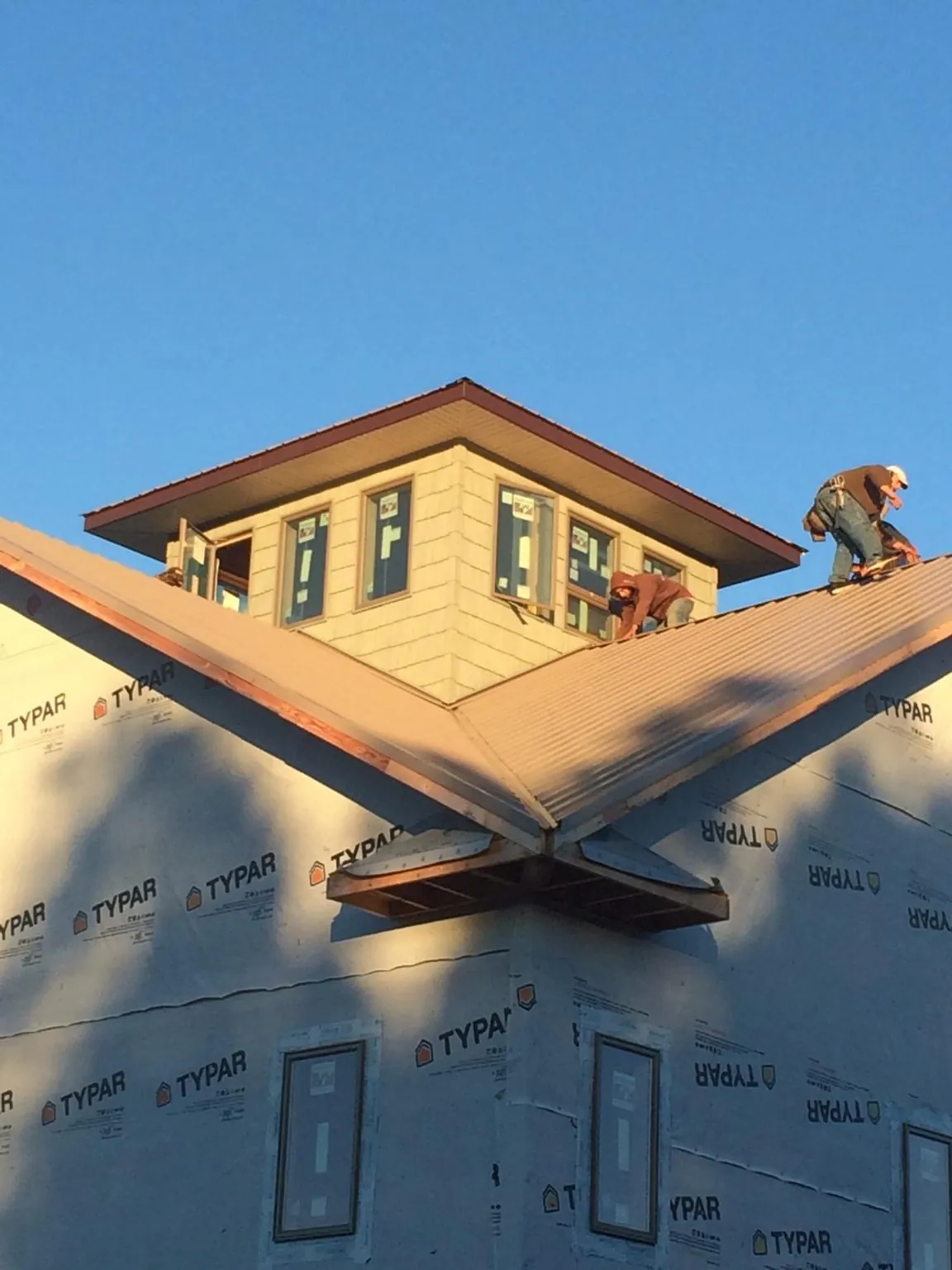 Roofers working around a rooftop cupola on a new metal roof at sunset — Roof Waterproofing in Blanchard by Roofing Brothers